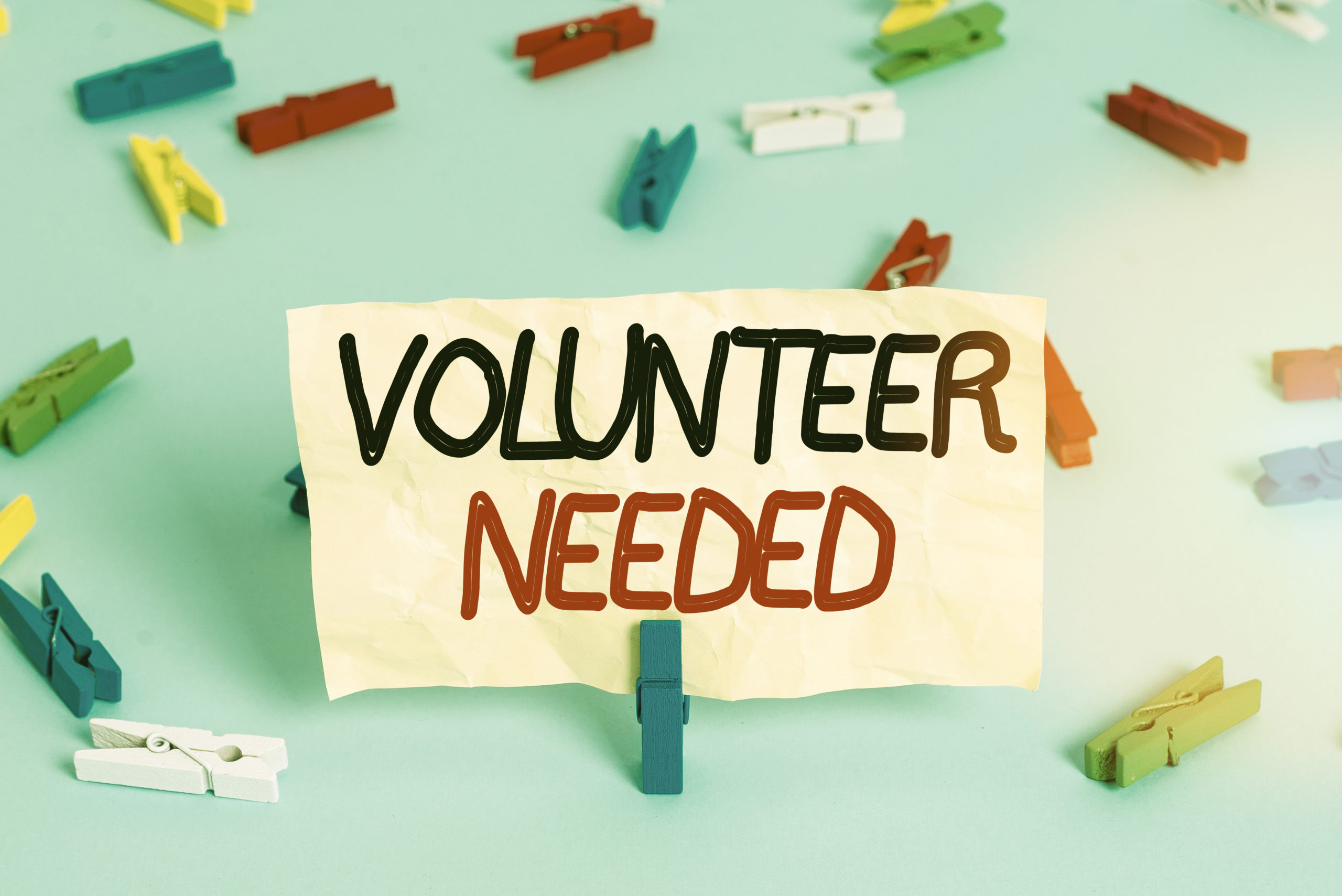 "Volunteer Needed" written on a piece of paper surrounded by clothespins